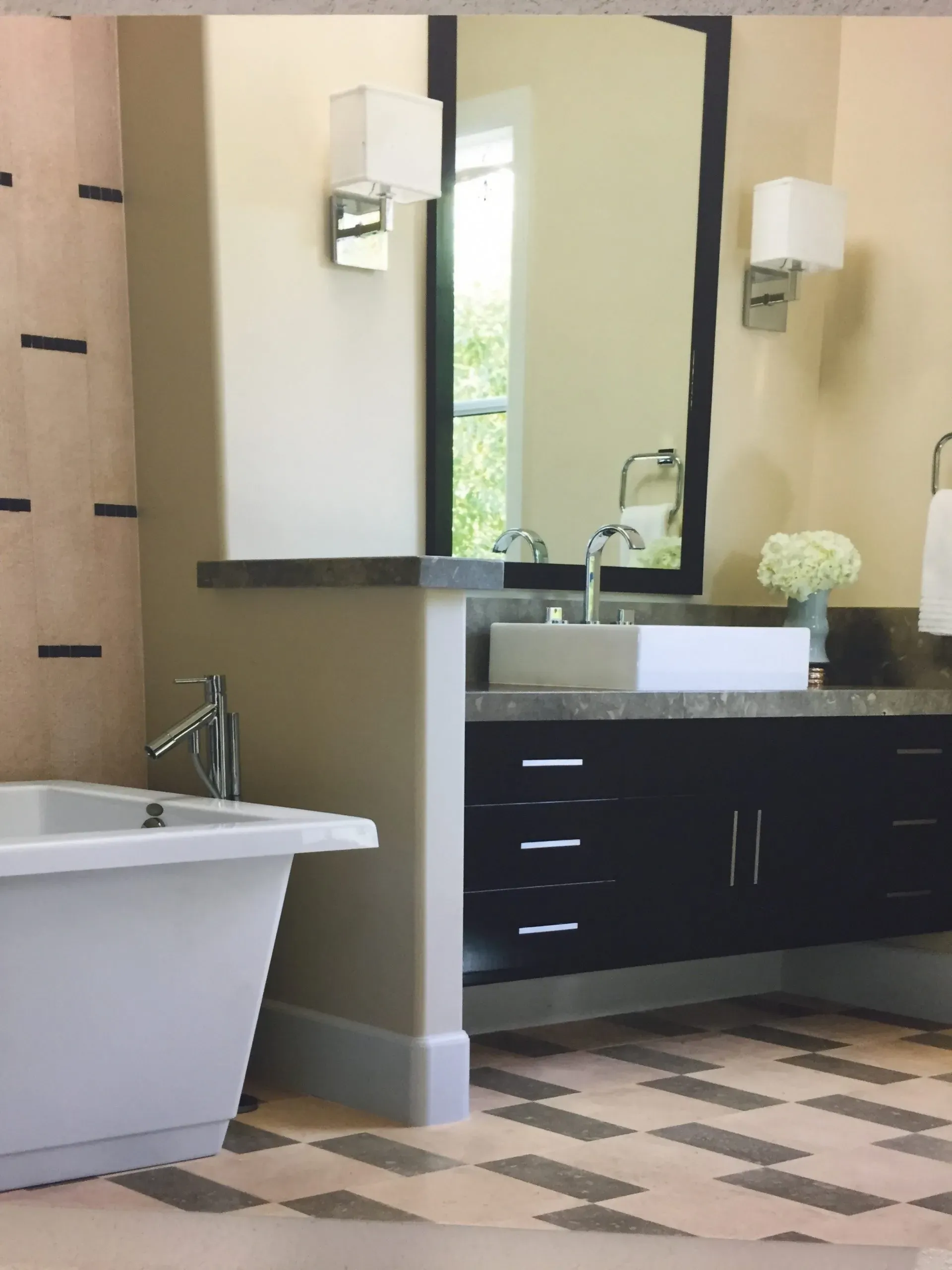 A modern bathroom designed by Green Living Builders LLC in Berkeley, featuring a sleek bathtub, dark vanity with under-counter storage, large mirror, and geometric-patterned floor.