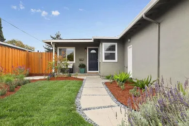 Front view of a house with a neatly landscaped yard, featuring green grass, decorative plants, and a freshly painted exterior wall.