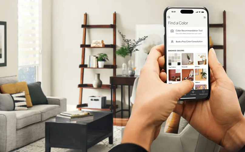 A person using a mobile phone app to explore color options in a modern living room, featuring a cozy sofa and bookshelf in the background.