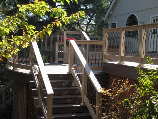 A well-crafted wooden deck with decorative railings, surrounded by trees, leading to a house.