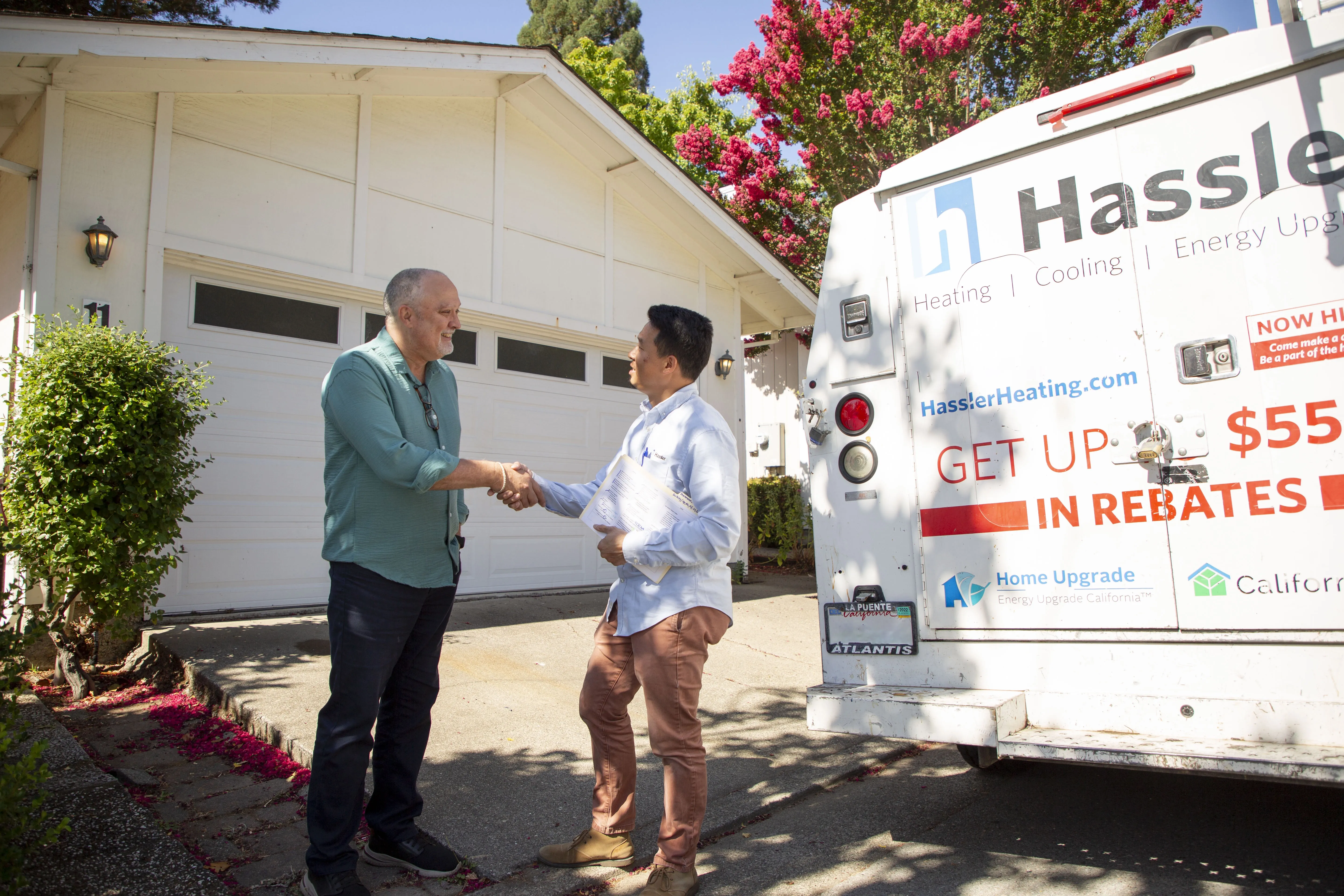 Two men shaking hands in front of a Hassler Heating & Air Conditioning, LLC service vehicle near a house in El Cerrito.