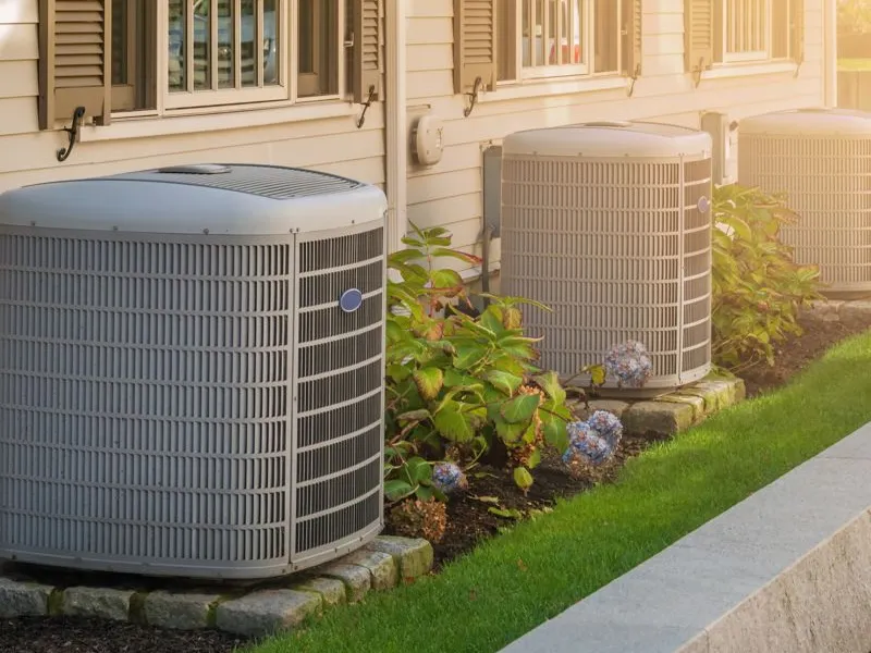 Three outdoor HVAC units installed alongside a house, surrounded by landscaping, representing the quality service provided by Hassler Heating & Air Conditioning, LLC in El Cerrito.