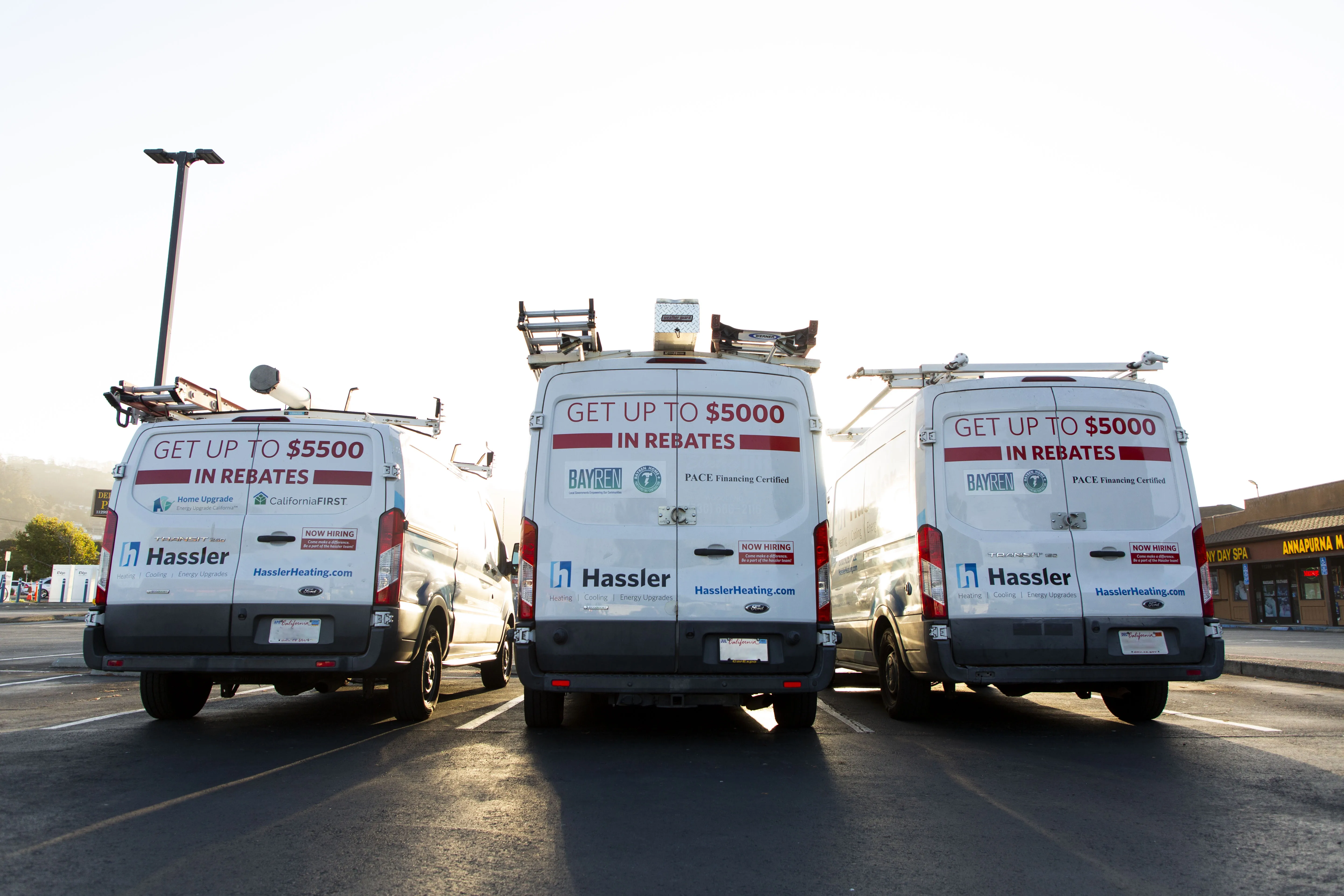 Three Hassler Heating & Air Conditioning, LLC vans parked in a row in El Cerrito, each promoting up to $5000 in rebates with clear branding and contact information.