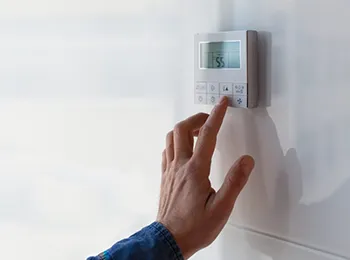 A person adjusting a digital thermostat on a wall, illustrating precise climate control.