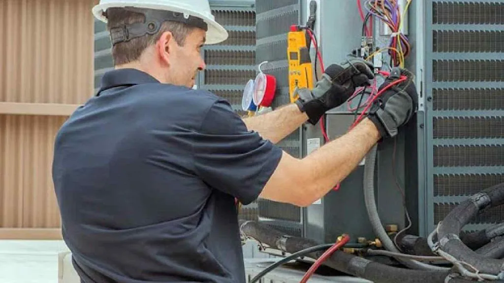 A technician from Heating And Air Experts in Fremont is servicing an HVAC unit, adjusting wires and using diagnostic tools.