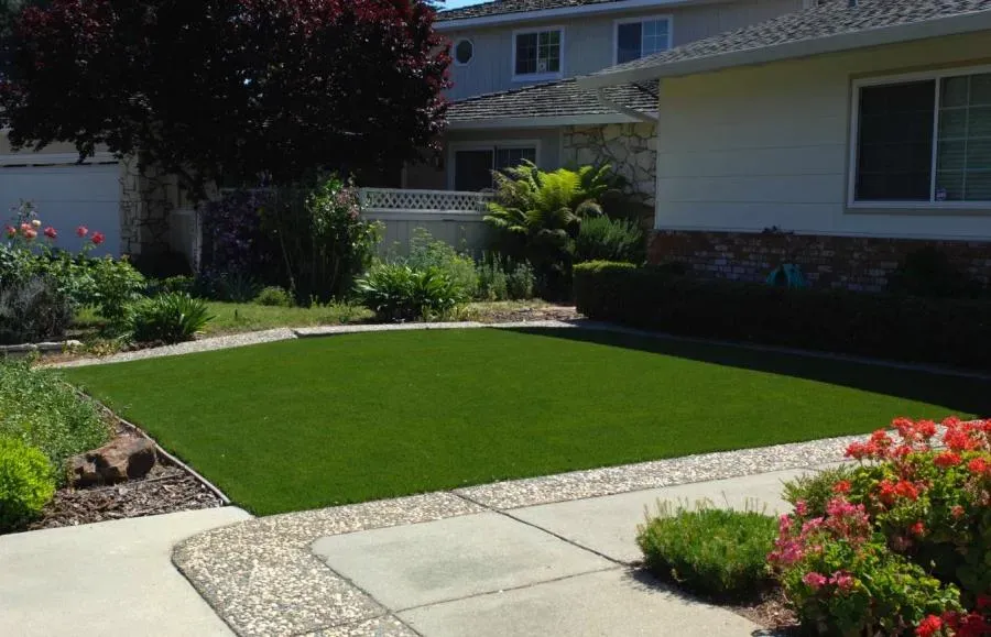 A well-maintained front yard with artificial grass from Heavenly Greens, surrounded by a variety of plants and a residential house in San Jose.