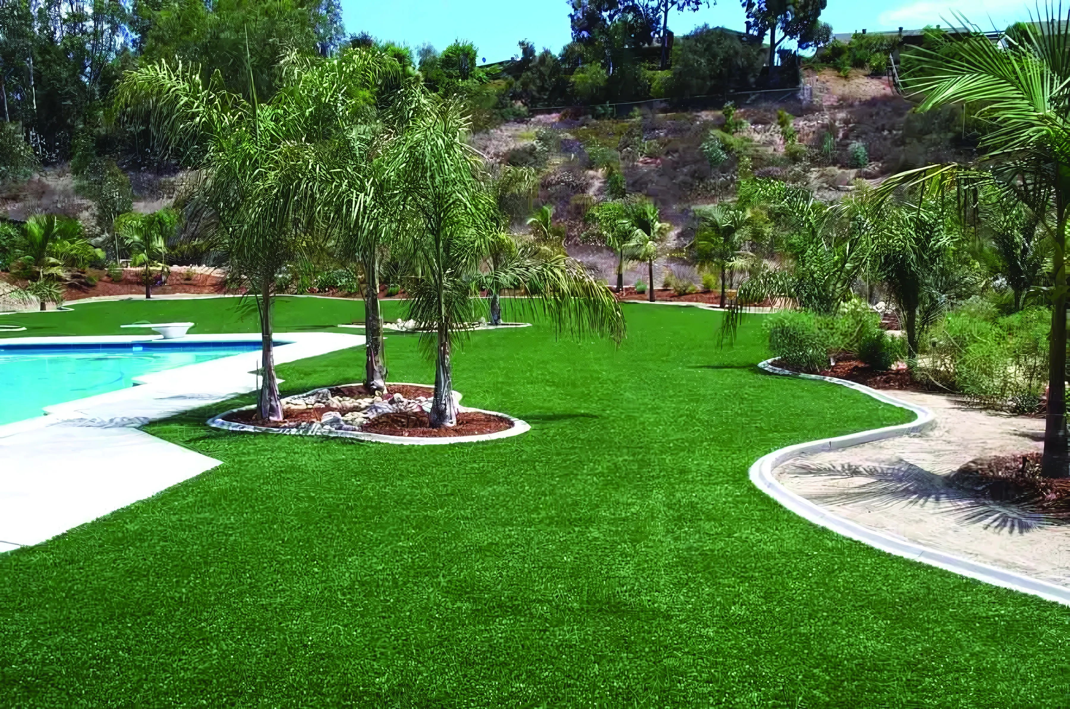 A well-maintained artificial grass yard with palm trees and a swimming pool, designed by Heavenly Greens in San Jose.