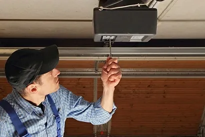 A technician in a cap and plaid shirt examines a garage door opener mechanism.