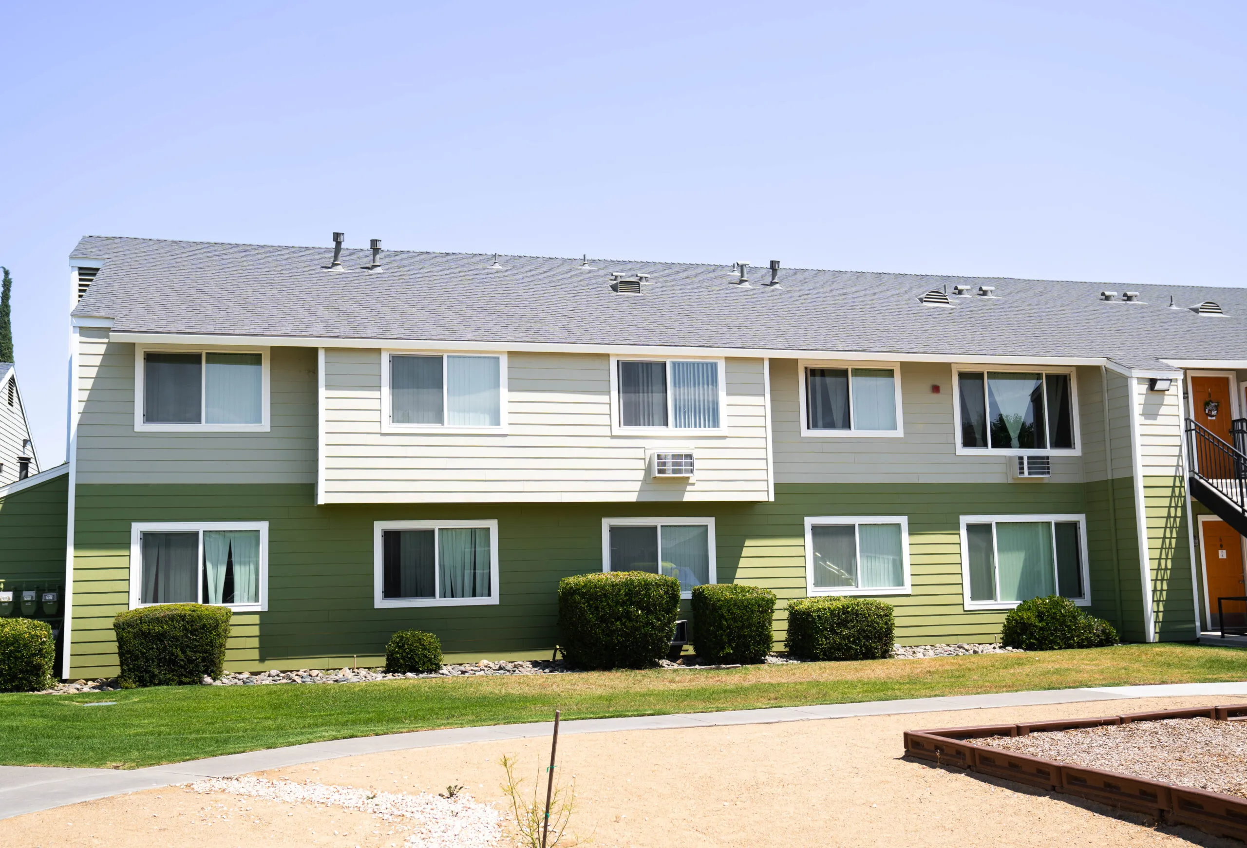 A two-story residential building with a green and beige exterior, featuring several windows and a neatly landscaped lawn, located in Sacramento.