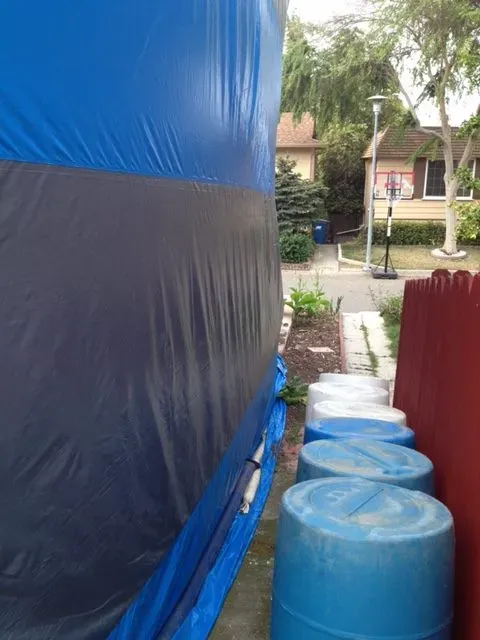 A building in Hayward covered with a fumigation tarp with blue barrels in the foreground, illustrating Hi Tech Termite Control of the Bay Area, Inc.'s professional termite treatment process.