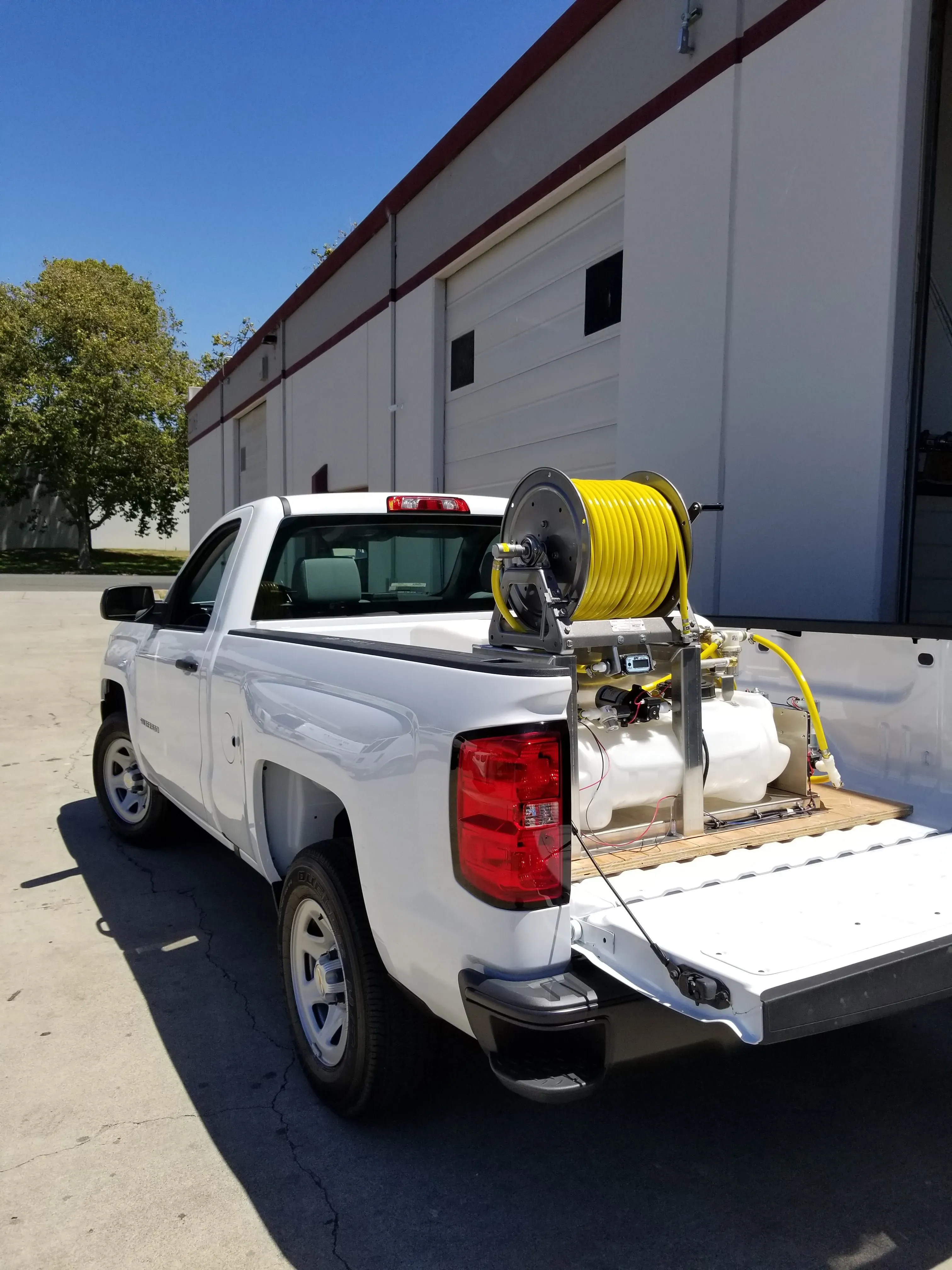 "A white service truck equipped with a hose and tank system, parked outside a warehouse, representing Hi Tech Termite Control of the Bay Area, Inc. in Hayward."