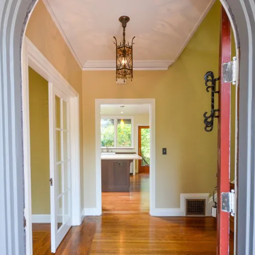 Interior view of a renovated home in Berkeley featuring polished wooden floors, a delicate ceiling light fixture, and an inviting kitchen seen through the doorway, completed by Home Healing Renovations, Inc.
