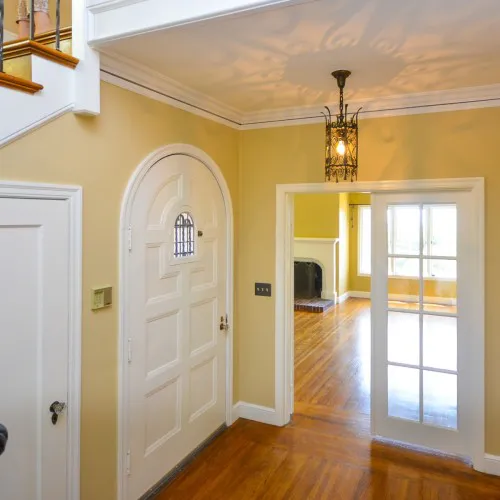 A beautifully renovated interior with a white arched door, glass-paneled door, polished hardwood floors, and a hanging light fixture, showcasing the work of Home Healing Renovations, Inc. in Berkeley.