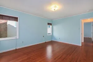 An empty, freshly renovated room with light blue walls and polished hardwood floors, featuring a central ceiling light and two windows.