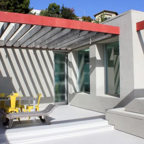 Outdoor patio with modern design featuring a pergola, yellow chairs, and a minimalist table in Berkeley, by Home Healing Renovations, Inc.