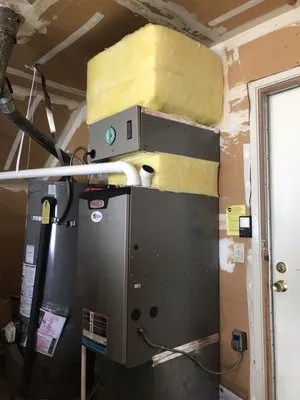 A heating and air conditioning unit installed in a garage, featuring insulation and pipes, representing the quality service offered by Hometown Heating & Air Conditioning in Concord.