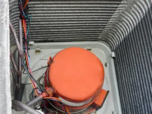 Close-up view of the inner components of an air conditioning unit, featuring wires and a central orange component.