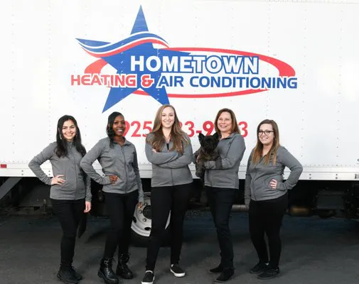 A group of five people from Hometown Heating & Air Conditioning pose in front of a company truck in Concord, all wearing matching gray jackets.