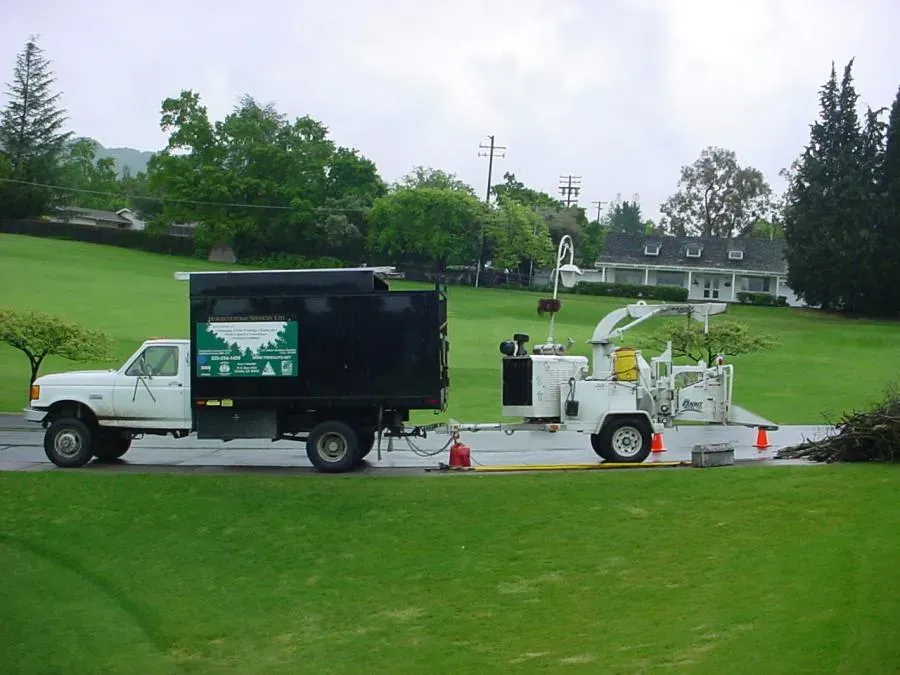 A landscaping truck and wood chipper operated by Horticultural Services, LTD in Orinda, parked on a residential street with green lawns and trees in the background.
