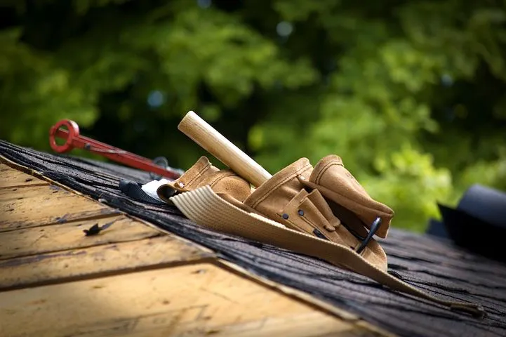 A tool belt with a hammer and tools on a rooftop, surrounded by greenery, representing the roofing work of ImRoofingCompany in Pacifica.