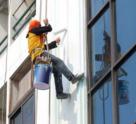 A professional painter from Innovation Painting Plus working on the exterior of a high-rise building in San Mateo, using ropes for safety.