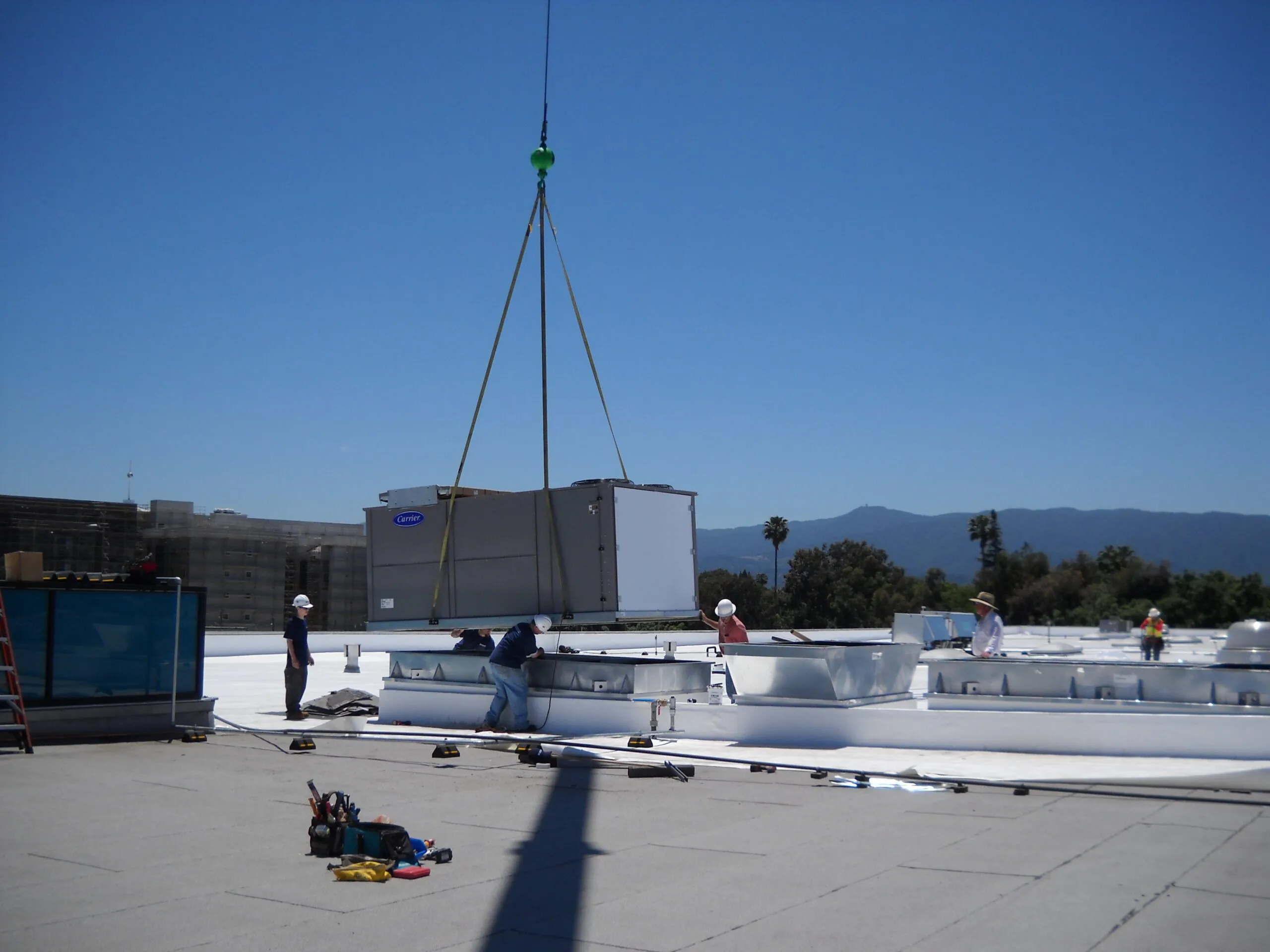 A rooftop HVAC installation by Innovative Mechanical, Inc. in South San Francisco, showing workers guiding a large unit being lowered by a crane.