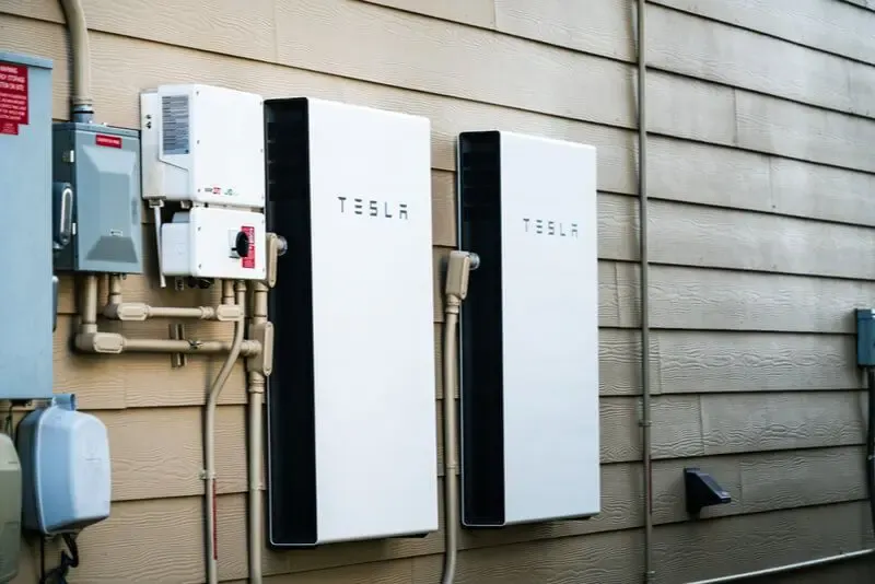Two Tesla Powerwall batteries mounted on the exterior wall of a building, showcasing a professional installation by Integrity Electric, Inc.