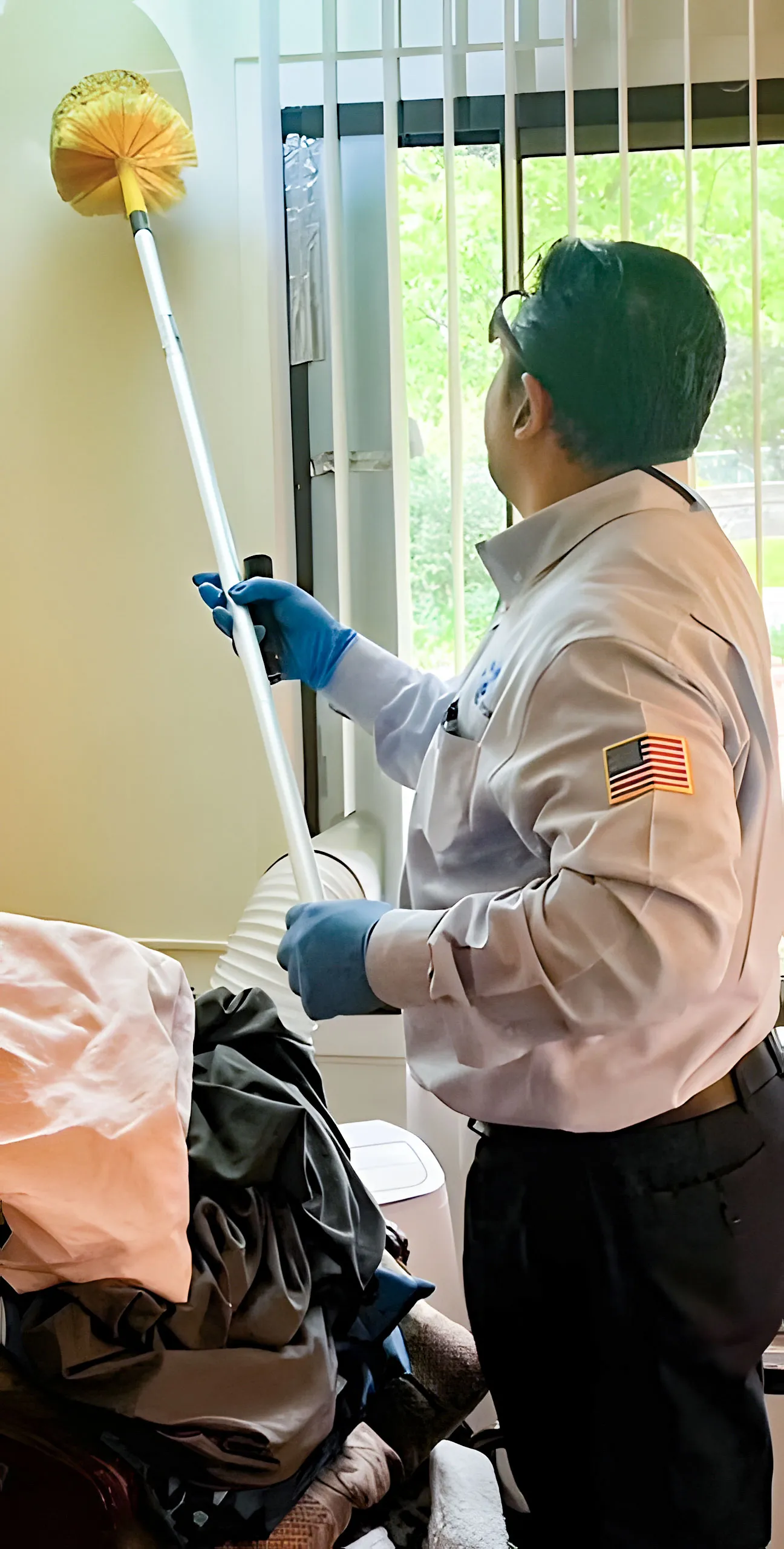 A pest control professional in uniform using a cleaning tool on a wall in a room, demonstrating the services of Intergrated Pest Control Management Inc. in Ontario.