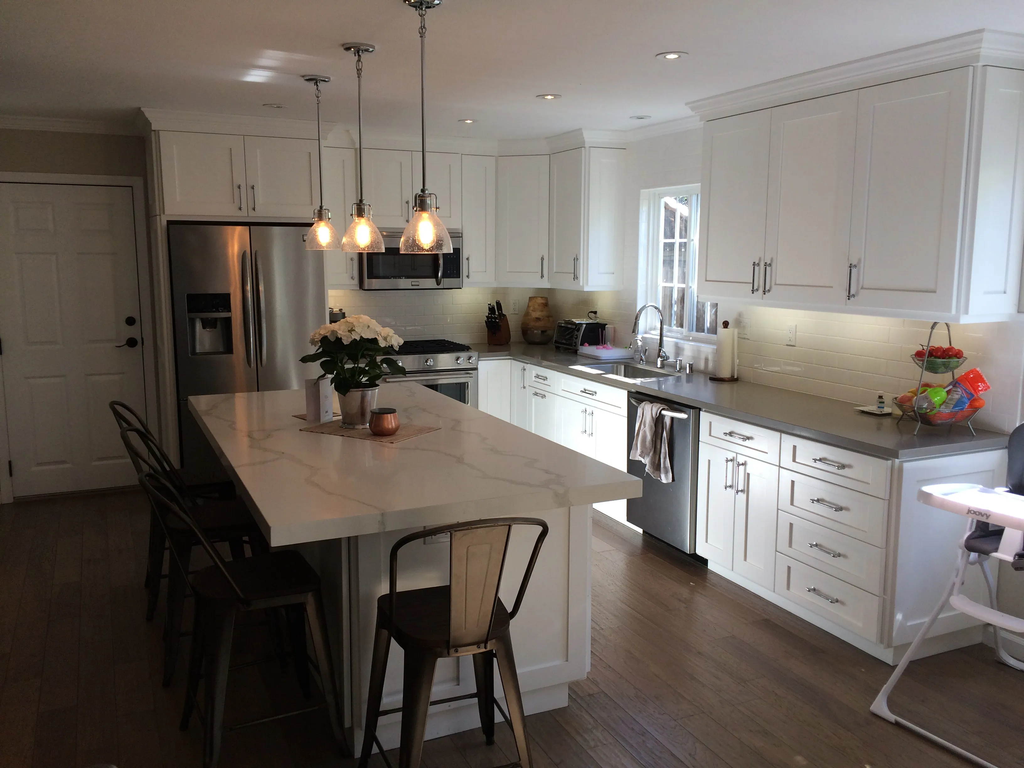 A modern kitchen with white cabinets, a large island with seating, stainless steel appliances, and pendant lights, designed by Irwin Construction Kitchen and Bath in Gilroy.