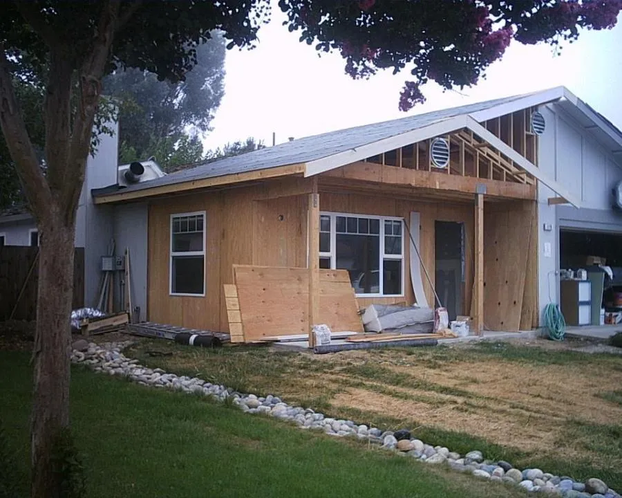 A house under construction with a new wooden facade, featuring large windows and a partially completed roof, by Irwin Construction Kitchen and Bath in Gilroy.
