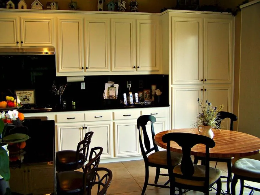 A modern kitchen with white cabinetry, black countertops, and a wooden dining table with black chairs, designed by Irwin Construction Kitchen and Bath in Gilroy.
