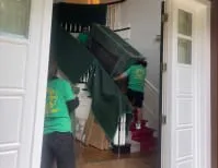 Movers from JC Express Movers carefully maneuver a large green couch up a staircase in a Walnut Creek home.