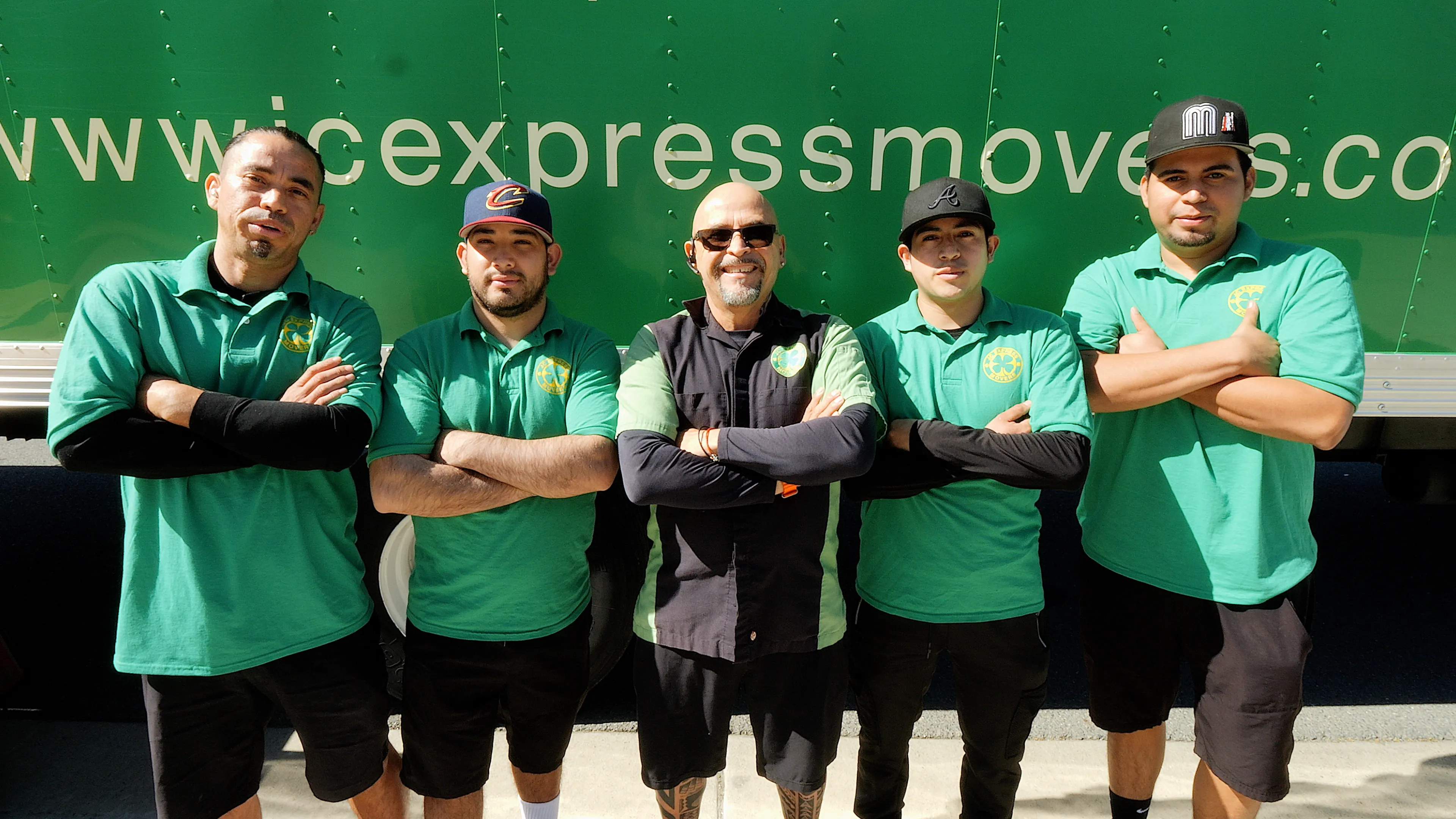 Group of five movers from JC Express Movers in Walnut Creek, standing confidently in front of a moving truck, wearing green shirts and smiling at the camera.
