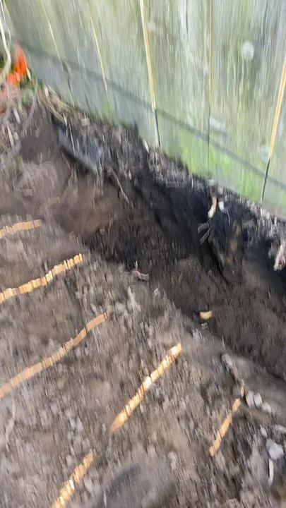 Image of a freshly dug trench beside a moss-covered wooden fence, illustrating groundwork by JV Gardening and Landscaping Inc. in Vallejo.