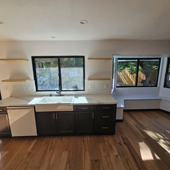 A modern kitchen with dark cabinets, hardwood floors, and large windows designed by J A SERRANO CONSTRUCTION in Santa Rosa.