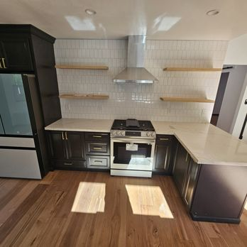 A modern kitchen with dark cabinetry, white countertops, and open wooden shelving, designed by J A SERRANO CONSTRUCTION in Santa Rosa.