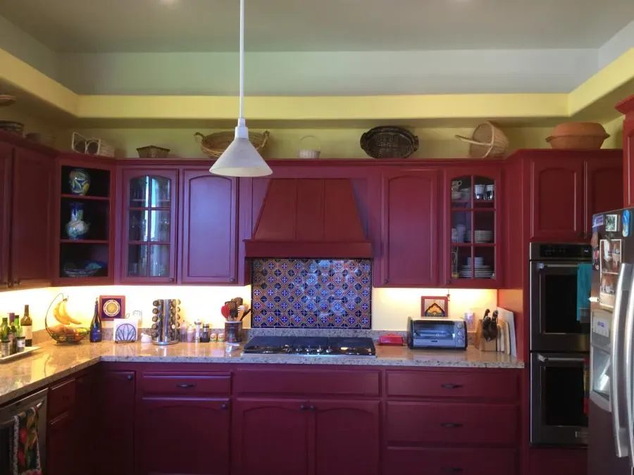 A kitchen with red-painted cabinets, a tiled backsplash, and modern appliances, showcasing the work of J & J's Final Coat Painting, Inc. in Concord.