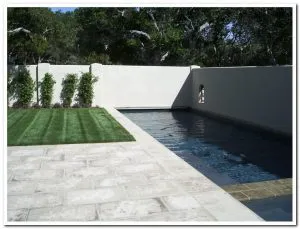 A landscaped garden featuring a neatly trimmed lawn, stone patio, and modern pool, designed by Jerry Allison Landscaping, Inc. in Watsonville.