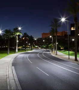 A well-lit, curved urban street at night with palm trees and illuminated buildings in the background, showcasing street lighting installed by Joe Lunardi Electric Company in Sebastopol.