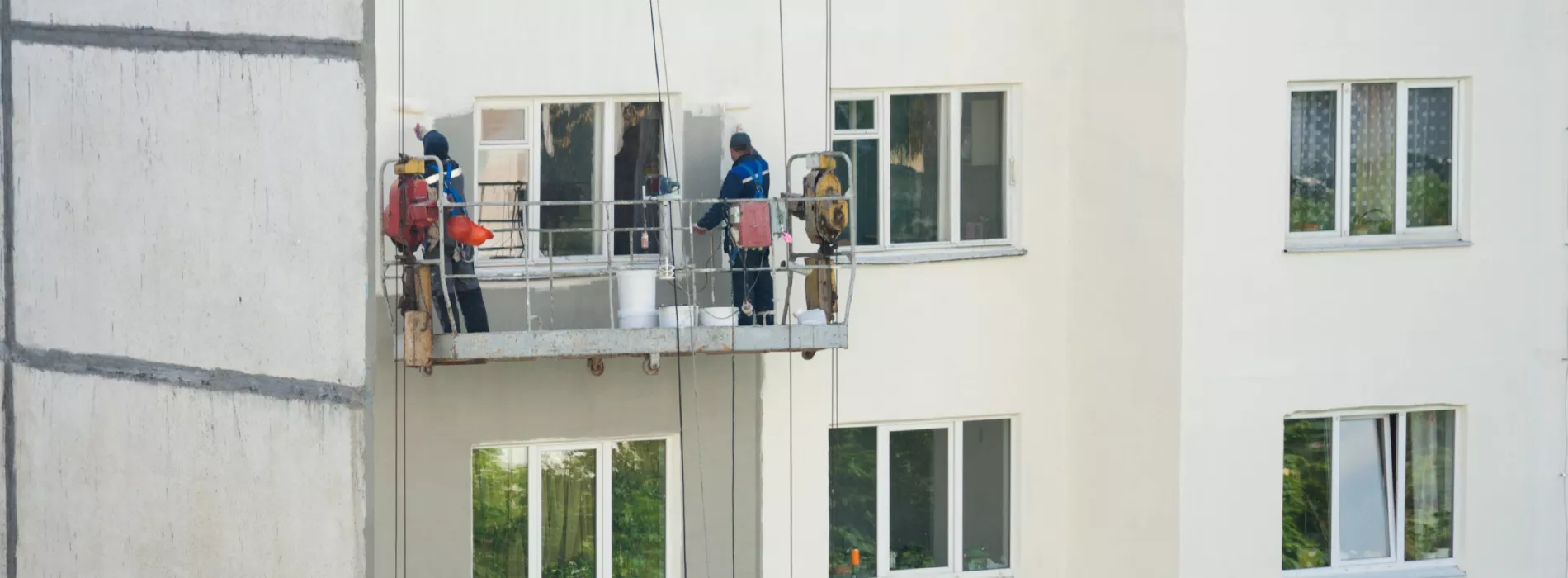 Two workers on a suspended platform painting the exterior of a multi-story building, part of Joe Moore Painting & Roofing's project in Windsor.