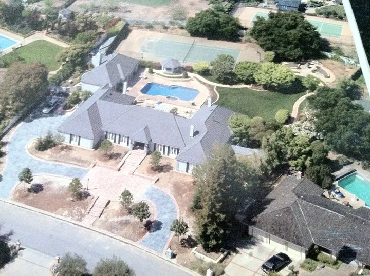 Aerial view of a large estate featuring a central building, circular driveway, swimming pool, tennis courts, and lush greenery, showcasing the quality work of John Casalegno Concrete Construction in Hollister.