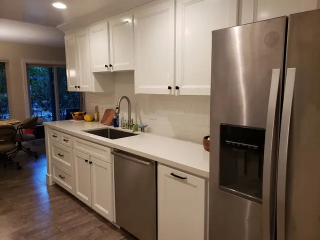 A modern kitchen with white cabinets, stainless steel refrigerator, and dishwasher, designed by Kaljian Construction Inc. in Concord.