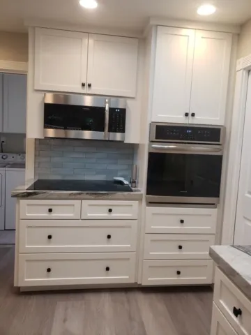 Modern kitchen with white cabinetry, a built-in microwave and oven, and a tiled backsplash, designed by Kaljian Construction Inc. in Concord.