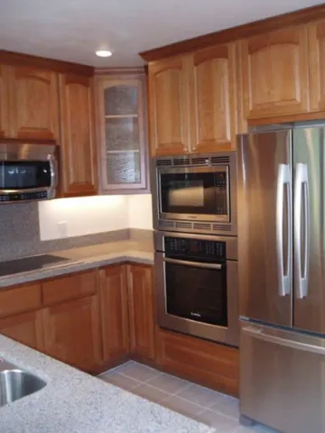 A modern kitchen designed by Kaljian Construction Inc. in Concord, featuring wooden cabinetry, stainless steel appliances, and granite countertops.
