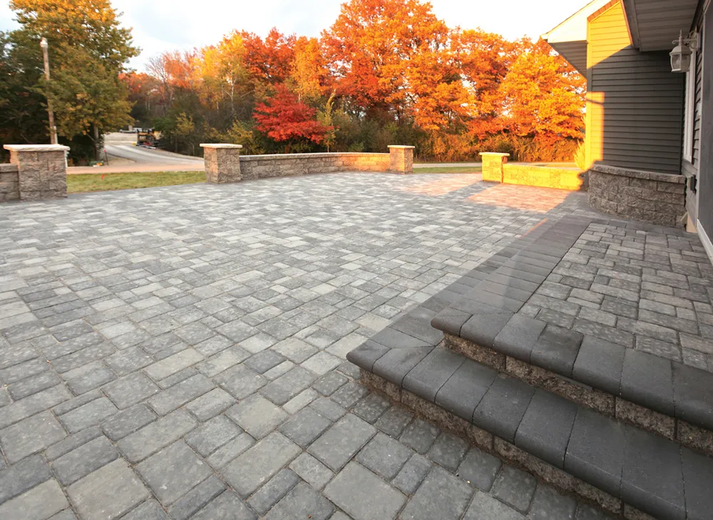 A paved patio area with stone steps and retaining walls, surrounded by autumn trees, created by Kodiak Construction in Martinez.