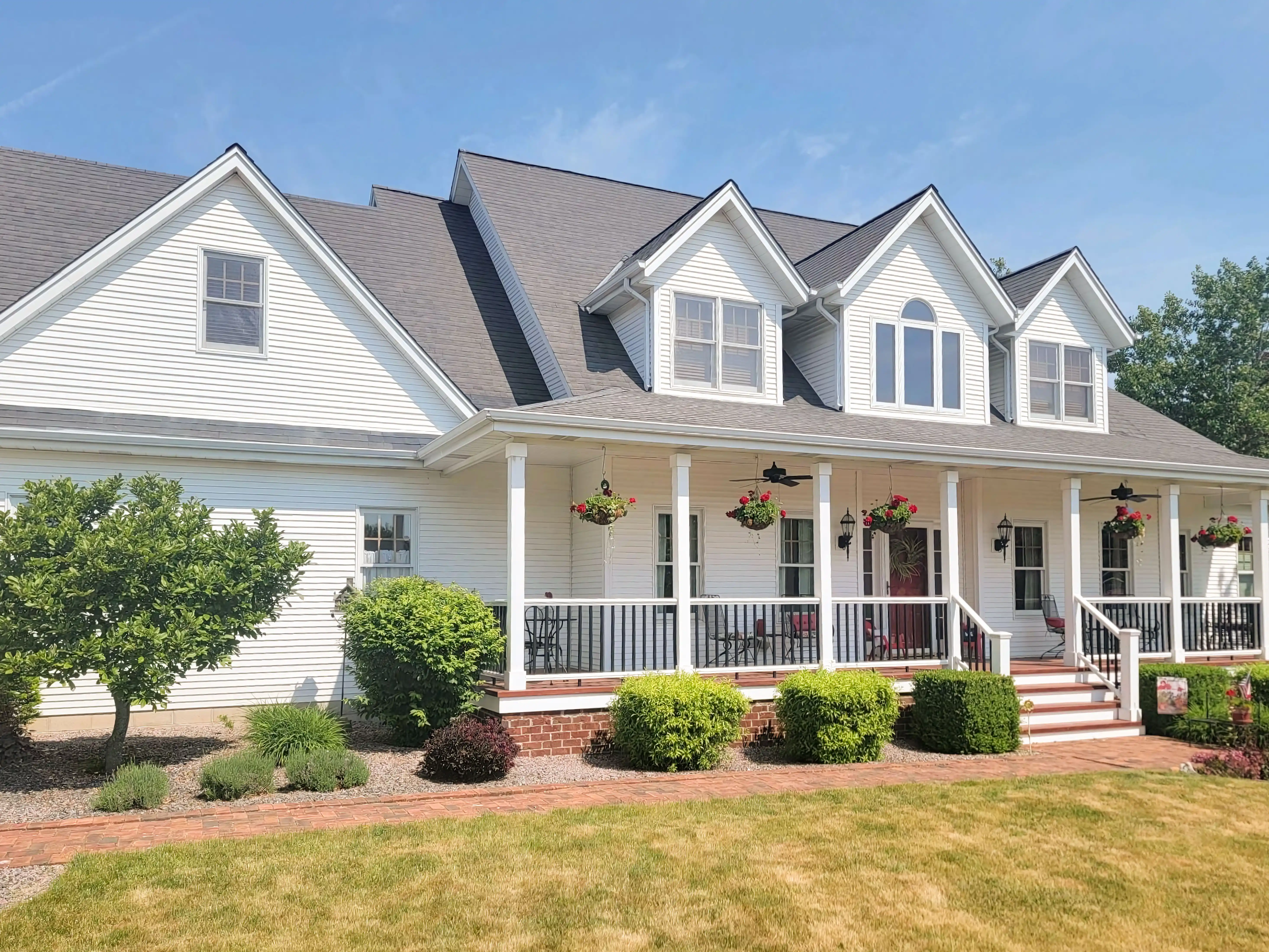A large white house with a front porch featuring columns and hanging flower baskets, surrounded by a neatly landscaped yard.