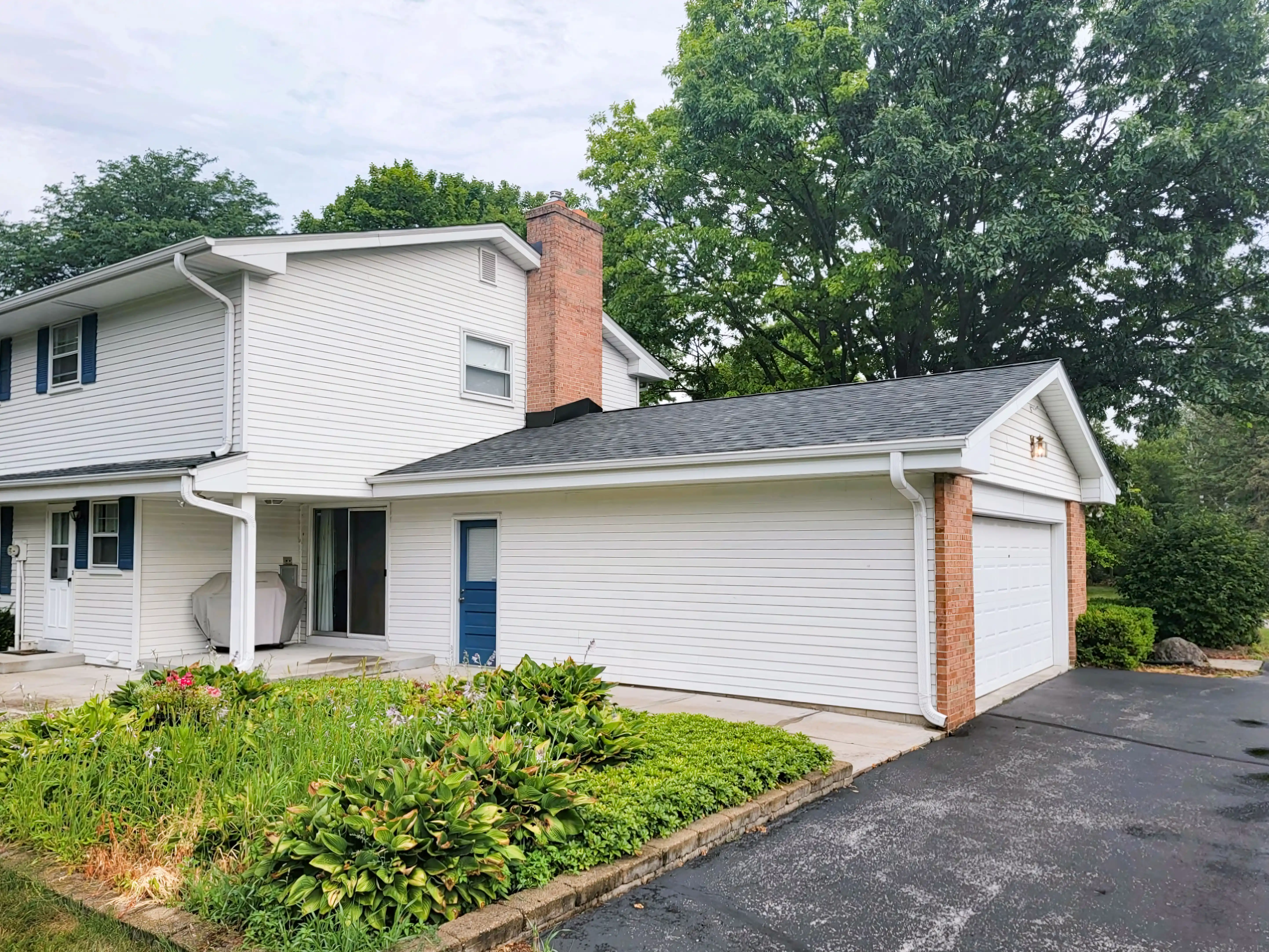 A two-story white house with a brick chimney and attached garage, surrounded by lush greenery, showcasing the quality craftsmanship of LJ Contractors in Franklin.