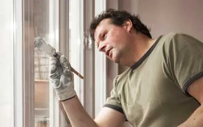 A person wearing gloves attentively paints a window frame, showcasing the skilled craftsmanship of LW Construction & Handyman Services in American Canyon.