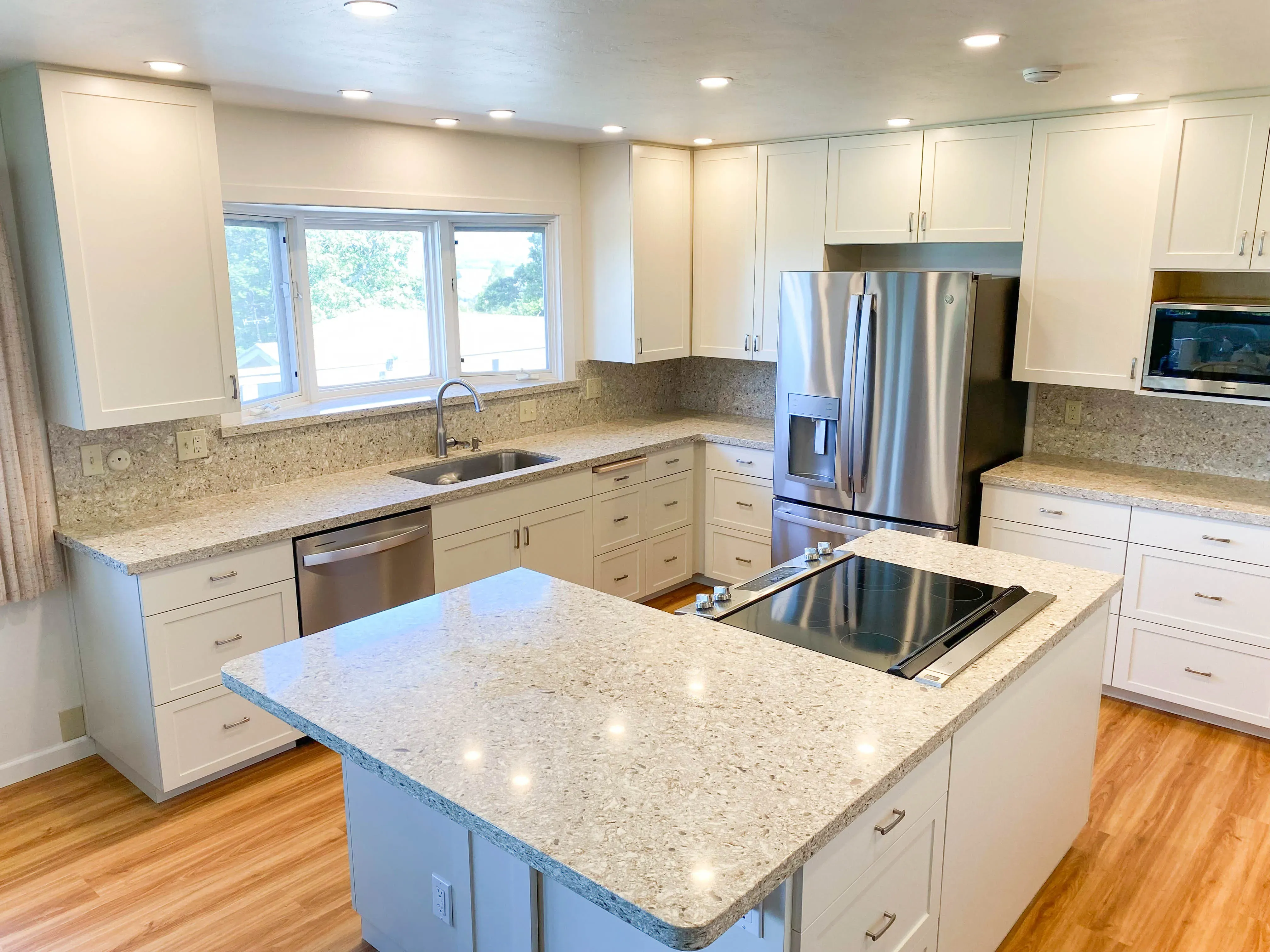 A modern kitchen remodel by Labourdette Construction in Sebastopol featuring white cabinetry, stainless steel appliances, granite countertops, and a central island with an induction cooktop.