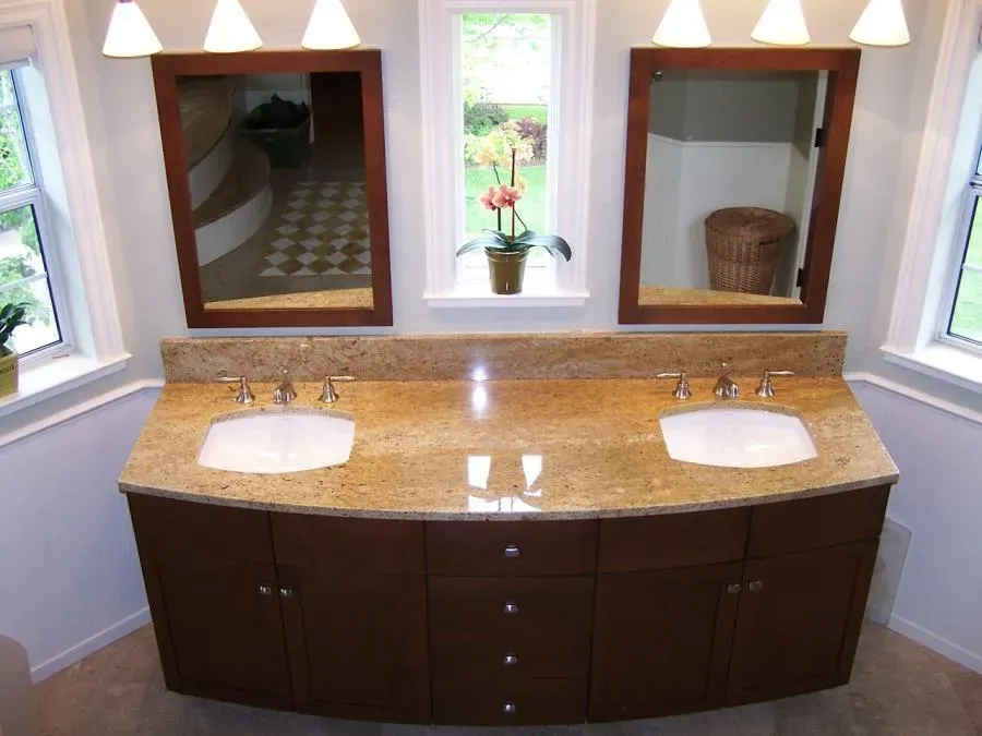 A double-sink bathroom vanity with a granite countertop, two wooden-framed mirrors, under-cabinet storage, and stylish lighting, designed by Labourdette Construction in Sebastopol.